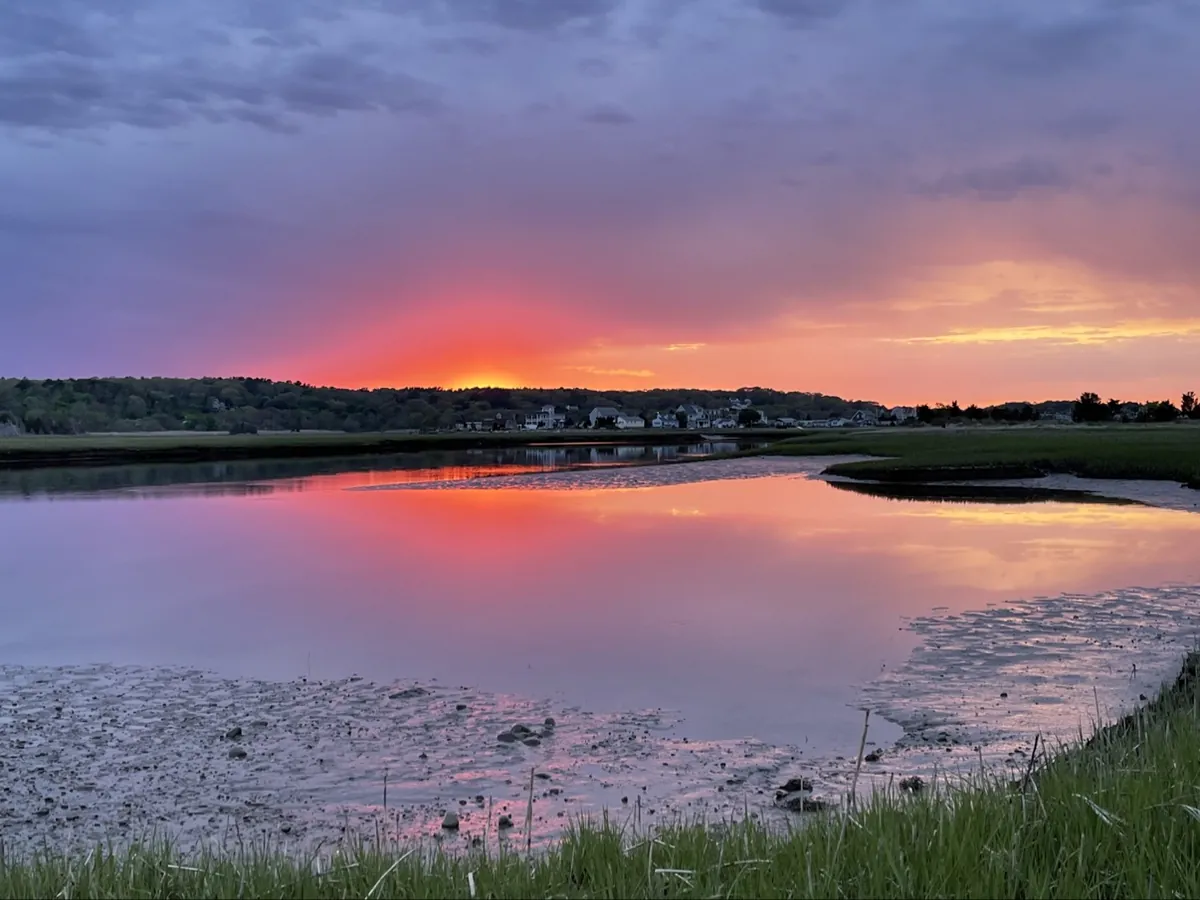 Sunset over the South River salt marsh in Marshfield, MA, seen from the Rexhame Beach parking lot — pink sky reflected in still water at low tide