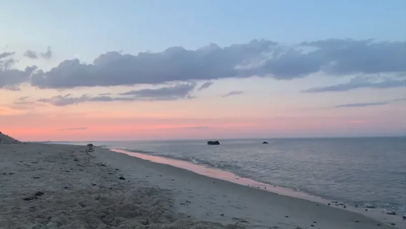 Sunset over Rexhame Beach in Marshfield, MA — pink sky over a quiet shoreline with rocks offshore